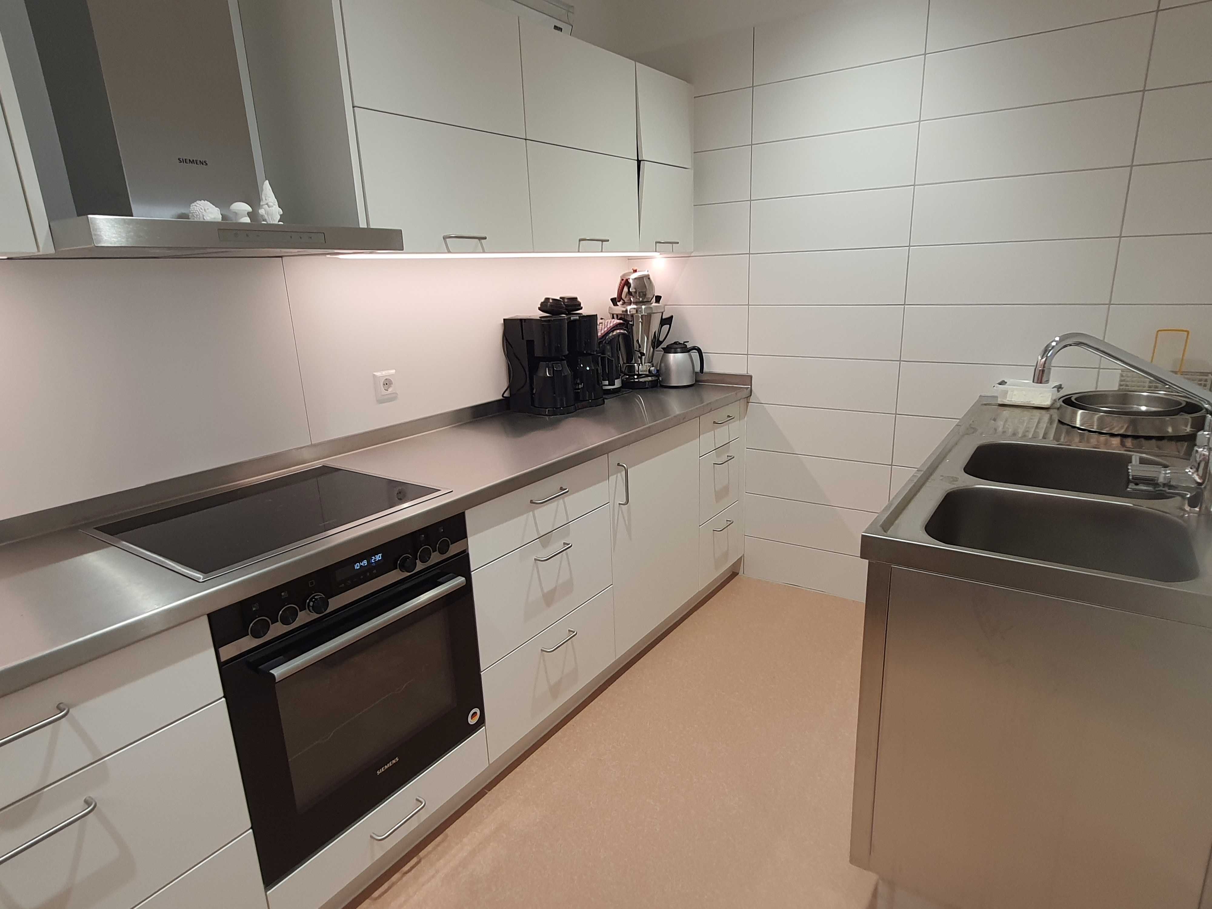 Küche mit Backofen, Herd, Schränken, Spüle, Kaffeenmaschinen und Kaffeekannen